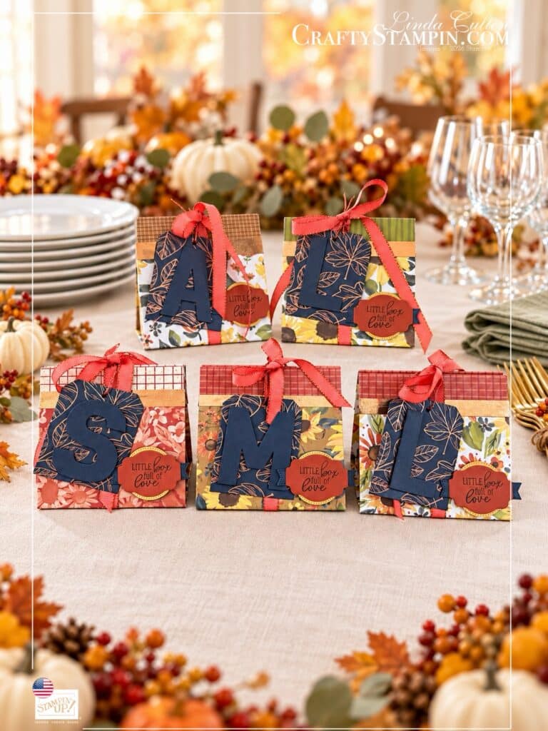 Five boxes with stacked plates and napkins Five Thanksgiving mini tea boxes with personalized monogram tags, autumn papers, and coral ribbon beside stacked plates and sage napkins.