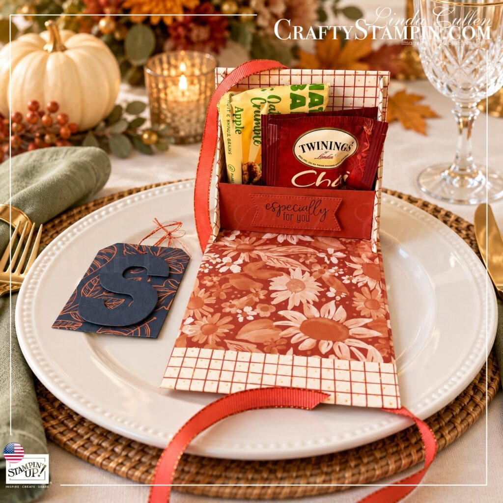 Open Thanksgiving tea box holding a Twinings Chai tea packet and an apple oat snack, with a floral fold-down cover and navy S tag beside it.