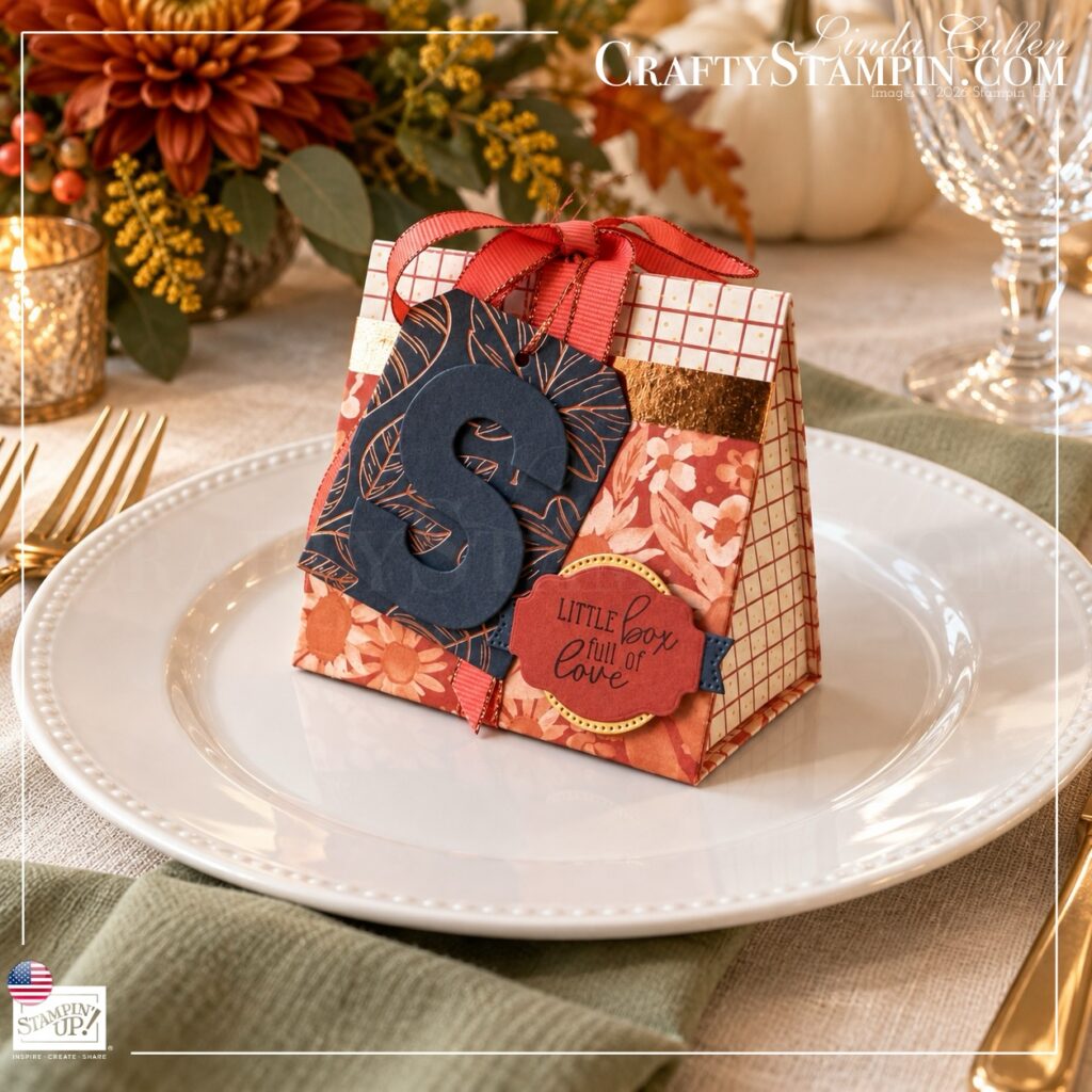 Side view of a Thanksgiving mini tea box on a dinner plate, showing its folded construction, patterned paper, and coral ribbon.